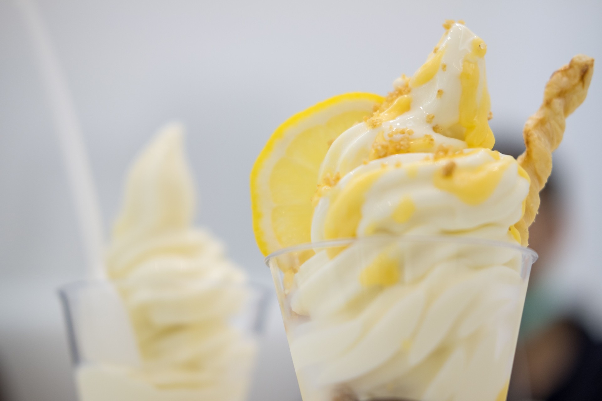 Lemon soft serve ice cream cone is shown with lemon slices and lemon sauce swirling around it served in cup