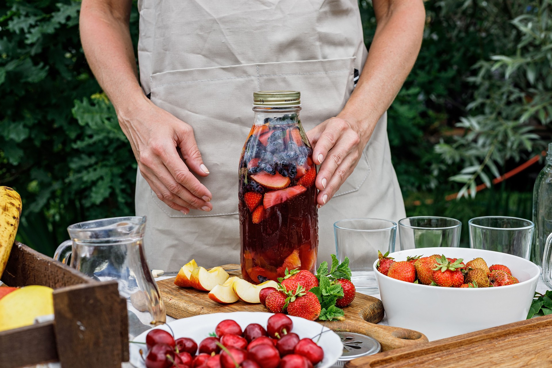 Woman hands hold a glass bottle with refreshing homemade lemonade or sangria punch with citrus fruits and organic berries. Summer cocktail with fruit juice and ice. Tasty cold sweet drinks.
