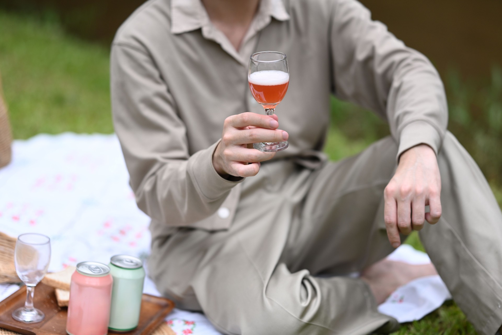 Close up image of A person holds a glass of sparkling drink, enjoying a peaceful moment during a picnic